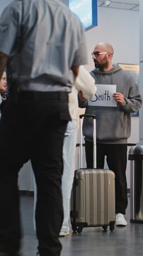 Airport Terminal: Airport Greeter Holding Name Sign, Meeting Passengers From Plane Flight. Diverse People Walking with Luggage. Business Transfer or Transportation Service. Full Shot. Vertical Shot.