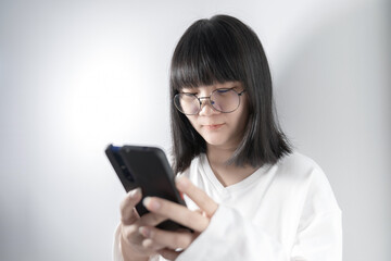 Isolated Pretty Asian glasses woman looks and holds mobile phone in her hand on white background in studio light.