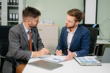 Two office colleagues discuss ideas for a startup project in a modern workspace, using laptops and smartphones