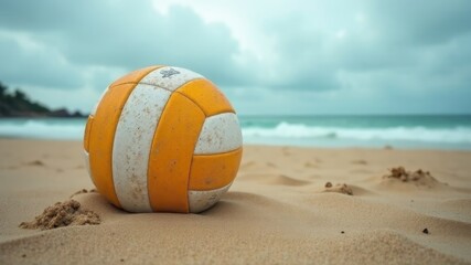 Close-up of worn volleyball on sandy beach with ocean waves in background.