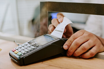 Close-up of a hand holding receipt next to a payment terminal during a transaction at a payment counter