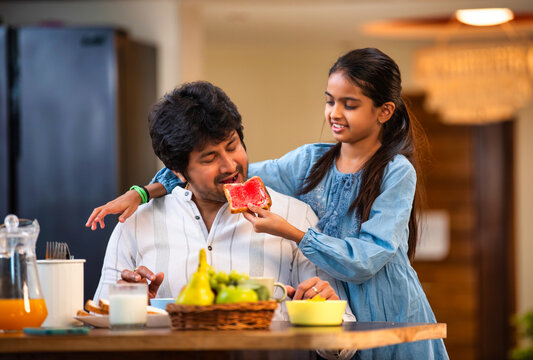Smiling Indian dad and daughter enjoy breakfast as she shares bread and jam, bonding over food