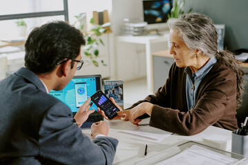 Obraz premium Two professionals in an office environment reviewing data on a tablet during a meeting session, one showing graphs and statistics, the other attentively listening and engaging