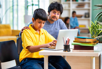 Father assisting young son with online learning using a laptop at home, focused on studies