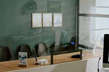 Modern banking reception area featuring sleek wooden counters and glass partitions, office decor includes framed images and contemporary table decor elements