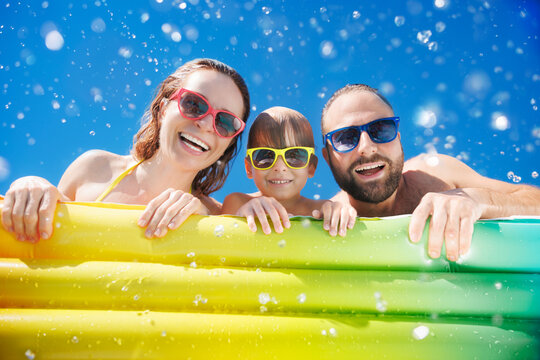 Happy family playing in waterpark. People having fun on summer vacation. Family jumping into swimming pool with splashes of water.