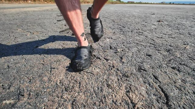 A man walks through mud and swampy cracked earth.