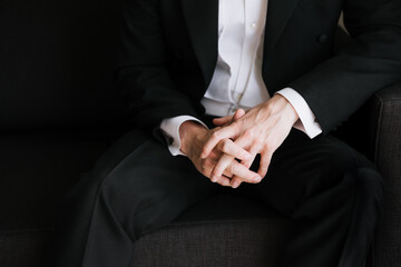 Obraz premium A man in a suit and white shirt is sitting with his hands folded