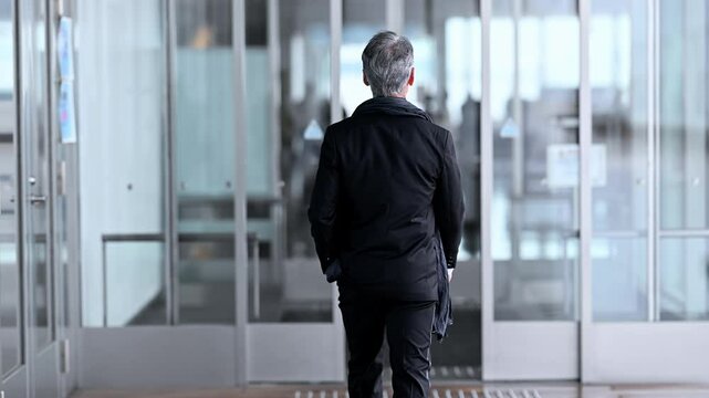 施設の自動ドアから屋外に出てくるタキシードを着た紳士