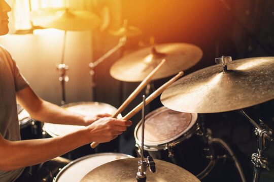 Drummer playing drum set in bright home studio with sunlight, concept of music performance, rhythm, percussion, musician lifestyle and sound production.