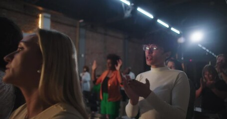 Worshipers at religious ceremony clapping hands, diverse group in spiritual moment, church setting, illuminated cross in background, joyful expression, focused on faith