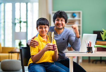 Indian Asian school boy proudly displays his trophy while father hugs him with joy and pride