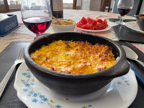 Pastel de choclo, platillo t&iacute;pico chileno en un librillo de greda, et&aacute; en una mesa bien servida junto a vino tinto y tomates.