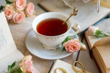 A cup of aromatic tea, a book and a rose on the table.