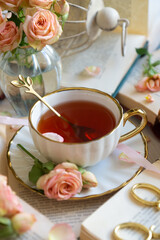 A cup of aromatic tea, a book and a rose on the table.