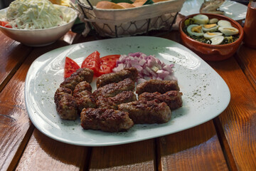Balkan cuisine. Cevapi - grilled dish of minced meat - with vegetables on rustic table