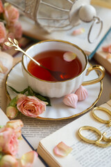 A cup of aromatic tea, a book and a rose on the table.