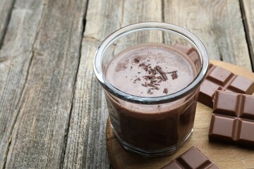 Tasty chocolate milk with shavings and pieces on wooden table, closeup. Space for text