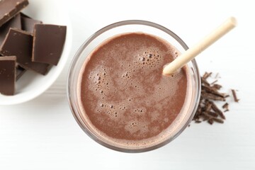 Tasty chocolate milk with shavings and pieces on white table, top view