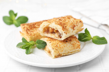 Tasty apple strudels and mint on white table, closeup