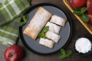 Tasty apple strudels with powdered sugar, mint and fruits on wooden table, flat lay