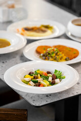 A close-up view of a vibrant salad with feta cheese, olives, and fresh vegetables, arranged on a table alongside other appetizing dishes, showcasing a healthy dining experience.
