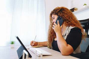 Focused businesswoman taking notes while talking on the phone in a modern office