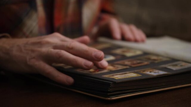 close-up philatelist examines and touches with his fingers his collection postage stamps in special collector's album. blurred view. hobby. front view.