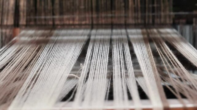 Detailed view of threads stretched across a loom, ready for the weaving process. The focus is on the parallel arrangement of the warp threads, their texture, and the structure of the loom.