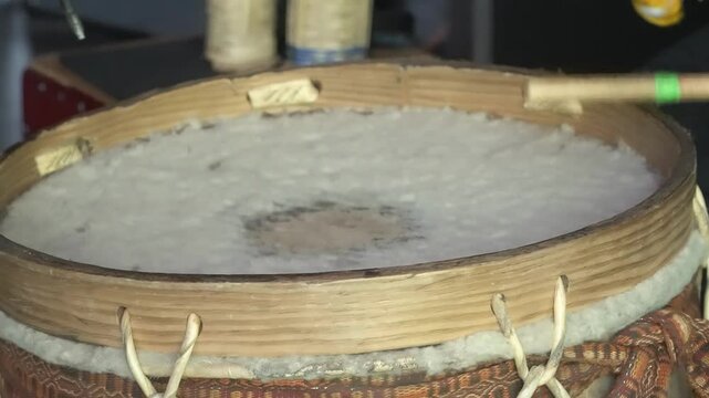 Close-up of a person playing a Bombo Leg&uuml;ero, a traditional South American drum. The focus is on the musician's hands striking the drum with wooden sticks, showcasing the rhythmic and dynamic 