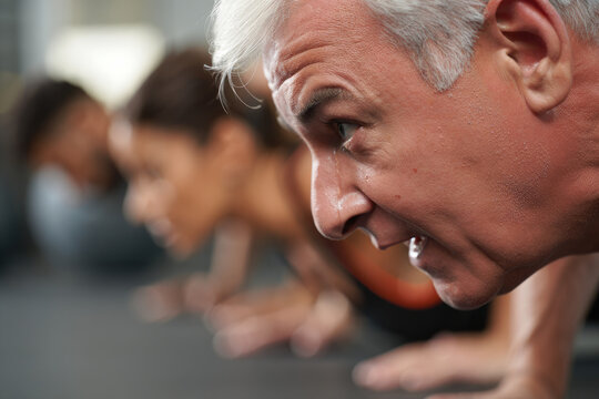 An elderly man is doing push-ups with other people in a gym, focusing on fitness and healthy lifestyle.