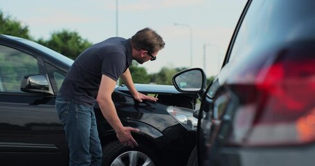 Young man in sunglasses sits stressed out after a car crash on the road. The concept of traffic accidents and insurance.