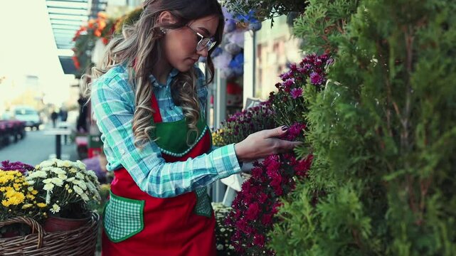 Beautiful young adult woman working in a street flower shop as a florist. Small business concept.