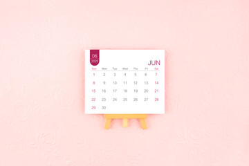 June 2025 calendar page with wooden easel on pink background.