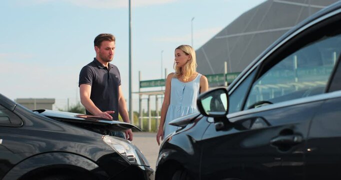 Drivers got into an accident and are standing near cars on the road. Two people man and woman talk argue on bad situation wait for the police outdoors.