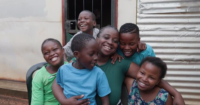 Poverty. Inequality. Portrait of a happy smiling black African woman and her children sitting in front of their shack in a township in Africa