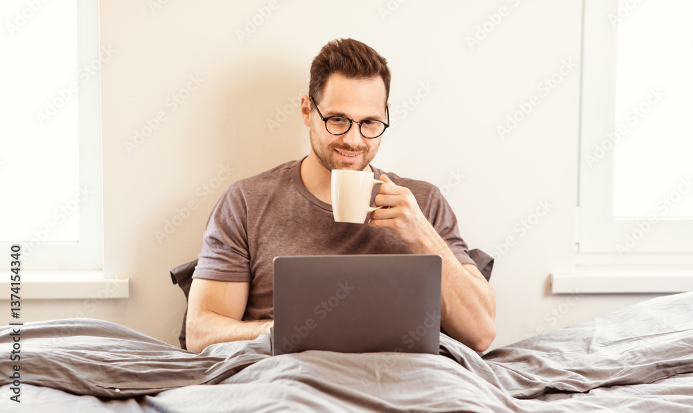 Poster man using laptop watching movie online drinking coffee sitting in bed in bedroom at home. guy at com
