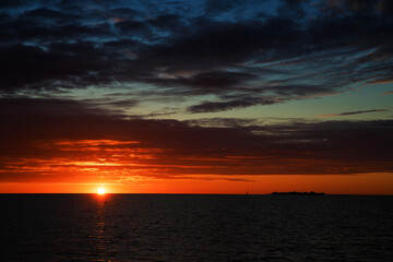 sunrise or sunset over the sea with brightly colorful clouds in the blue sky