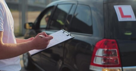 Closeup of instructor in driving school writing down results of exam. Driver courses, exam and people concept.