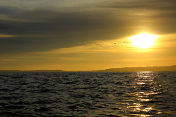 Obraz premium A stunning sunset photo captures the golden sky reflecting on the calm ocean, with a peaceful island beautifully silhouetted in the distance.