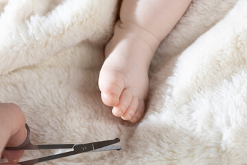 Mom trims baby's nails with baby scissors. Close up photo of mother's hands holding feet of the infant and nail scissors.