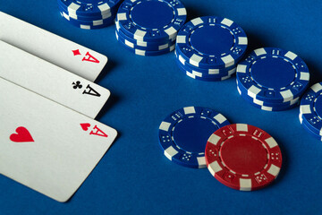 Obraz premium An exciting card game atmosphere with three aces and stacks of blue poker chips on a bright blue table during an evening gathering