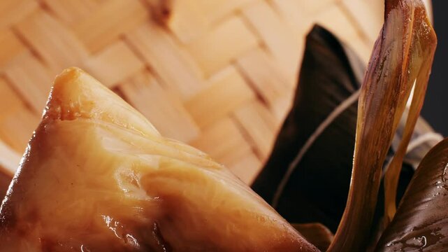Hand holding zongzi (rice dumpling) with savoury fillings wrapped in bamboo or reed leaves.