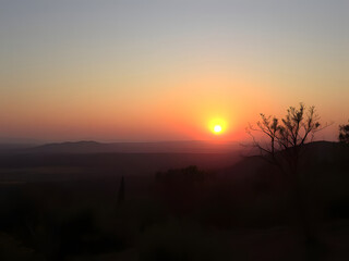 Fototapeta premium Stunning Sunset Over Hills and Horizon, Nature's Beauty, Orange Sky, Silhouette of Tree and Landscape.