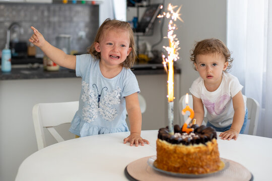 Two young children react to a birthday cake with sparklers. One girl looks excited, while the other appears scared and crying. A dramatic moment at a child's birthday celebration...