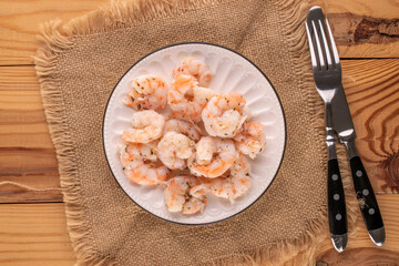Seafood salad, shrimp with garlic on a ceramic plate with a knife and fork, with a jute napkin on a wooden table, close-up, top view.