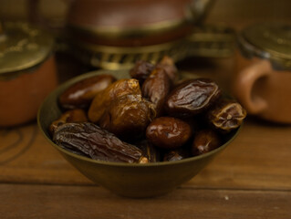 Dates in brass bowl wooden surface no people warm lighting traditional Middle Eastern setting