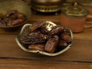 Dates in brass bowl wooden surface no people warm lighting traditional Middle Eastern setting