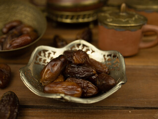 Dates in brass bowl wooden surface no people warm lighting traditional Middle Eastern setting