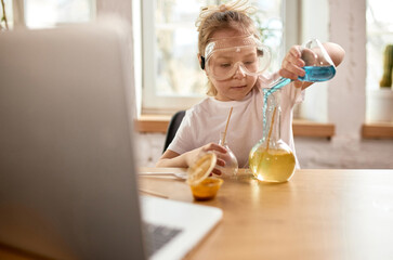 Girl pouring blue liquid into yellow solution with full focus during home science experiment inspired by online lesson. Concept of childhood, online education, remote studying